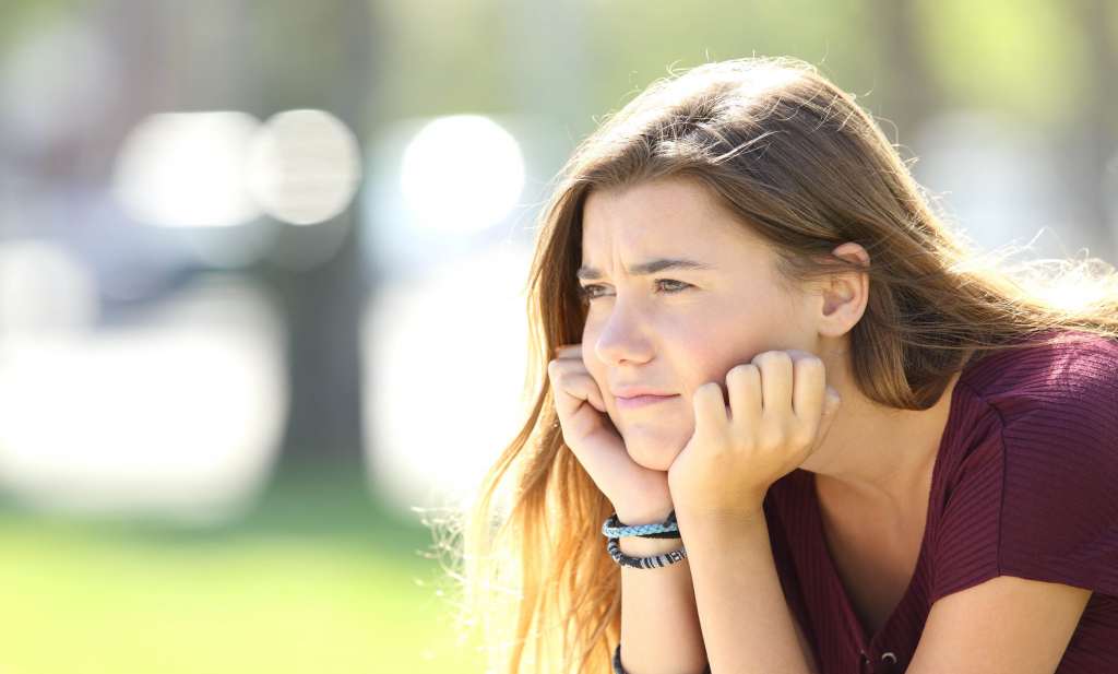 Portrait of angry teen looking sitting alone outside in a park