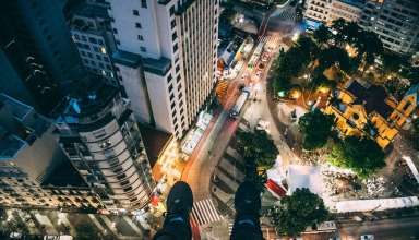 Man Sitting on High Rise Building Taking Photo Below Wallpaper